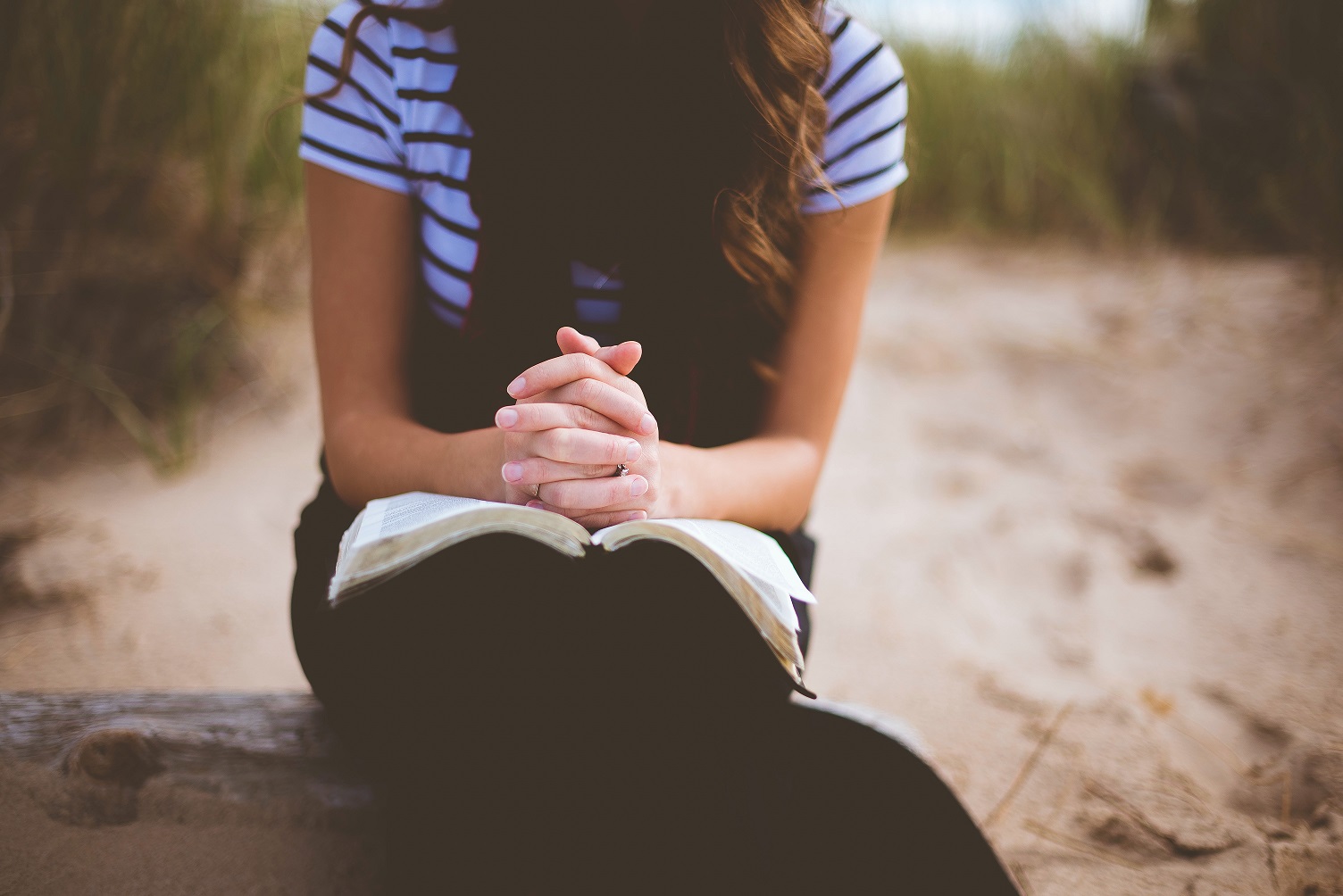 Woman praying with her hands on the Bible in an article by Dr. Jim Walkup on Spirituality in Counseling.